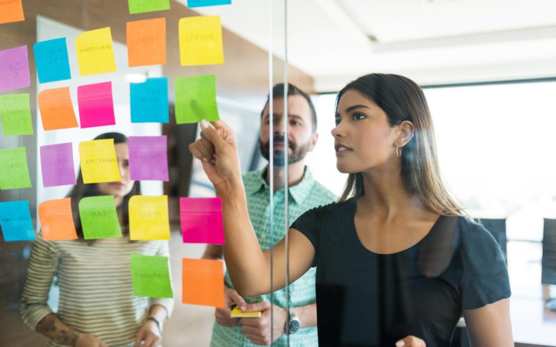 Female young manager discussing over adhesive note with coworkers in office meeting